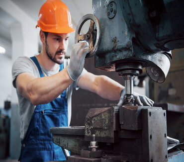 Portrait of a young worker in a hard hat at a large metalworking plant. The engineer serves the machines and manufactures parts for gas equipment.